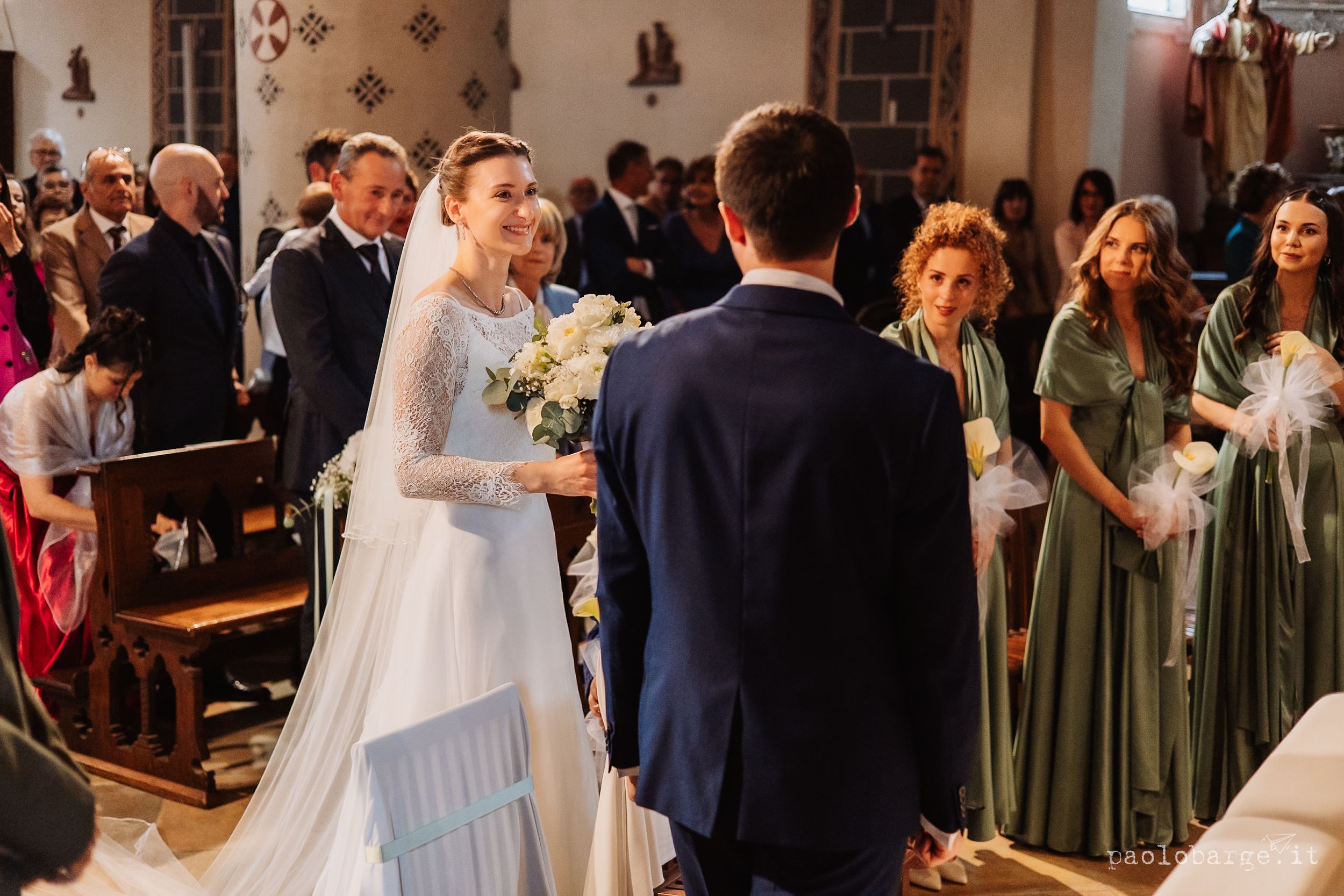 A wedding ceremony takes place in a traditional church with people in green bridesmaid dresses and formal attire.