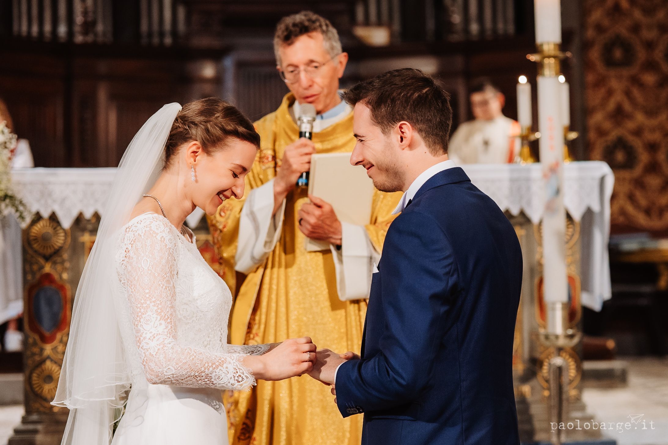 Bride and groom exchange rings during traditional church wedding ceremony with priest in gold robes.