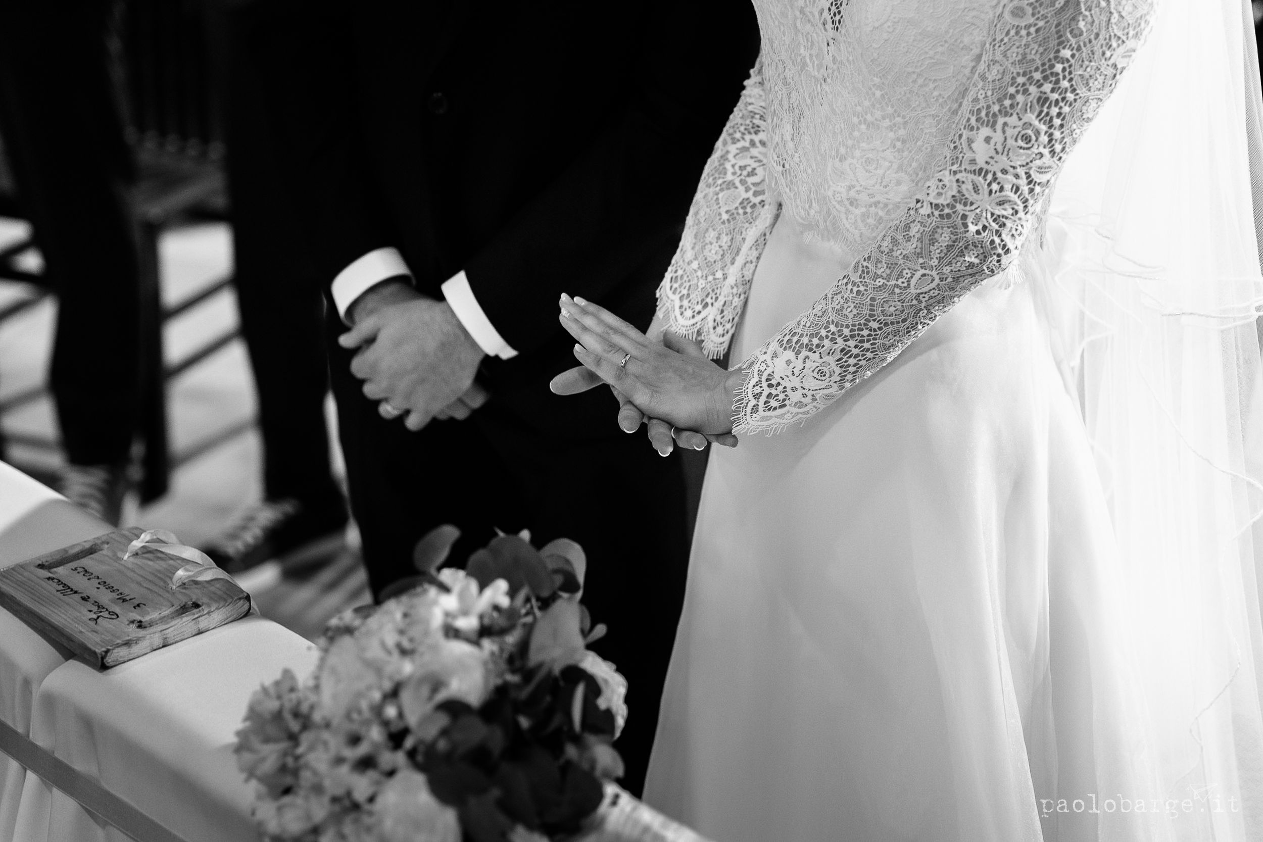 Black and white closeup of couple at wedding ceremony with bouquet and hands clasped during matrimonial blessing.