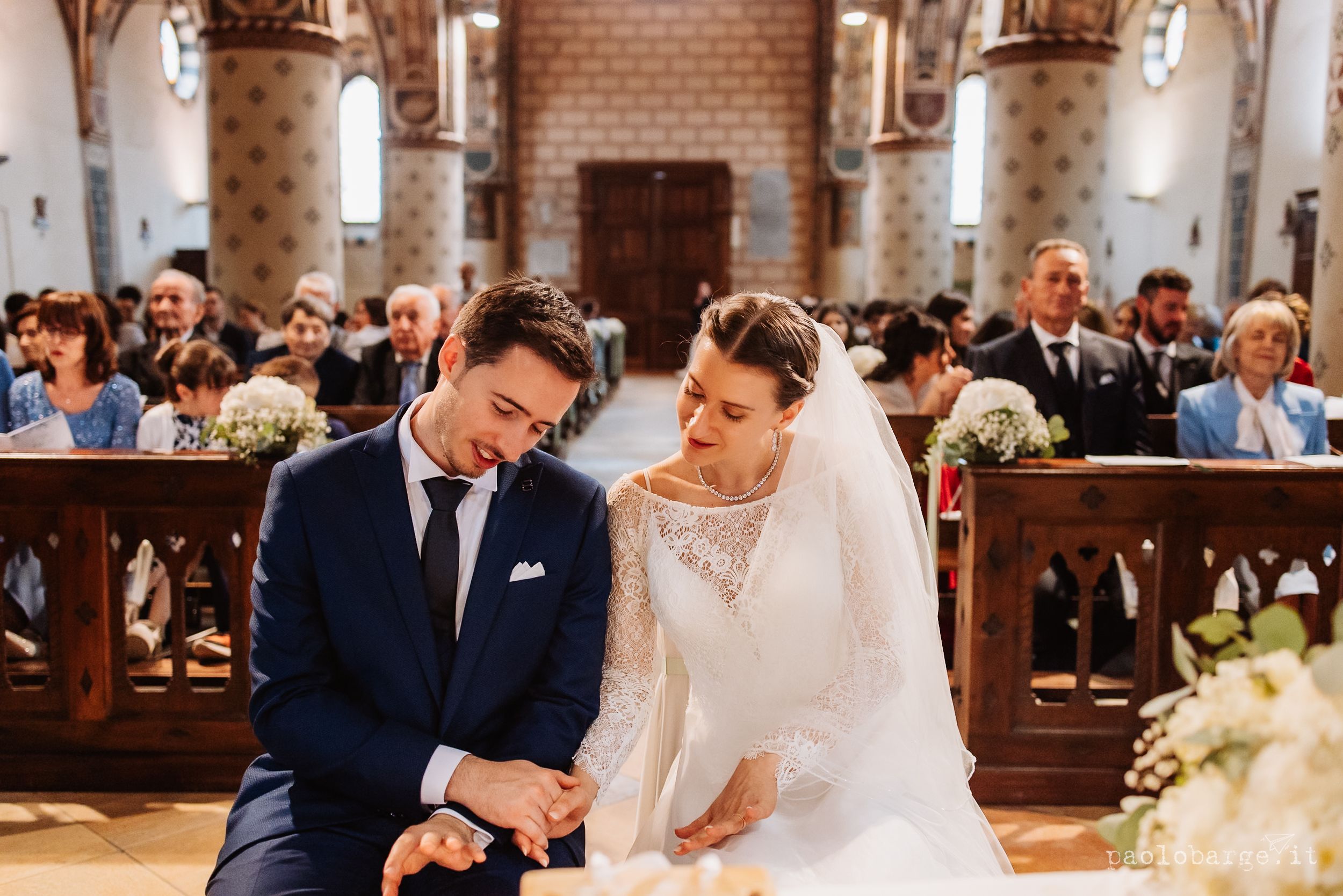 A couple shares a tender moment during their traditional church wedding ceremony with white floral decorations.
