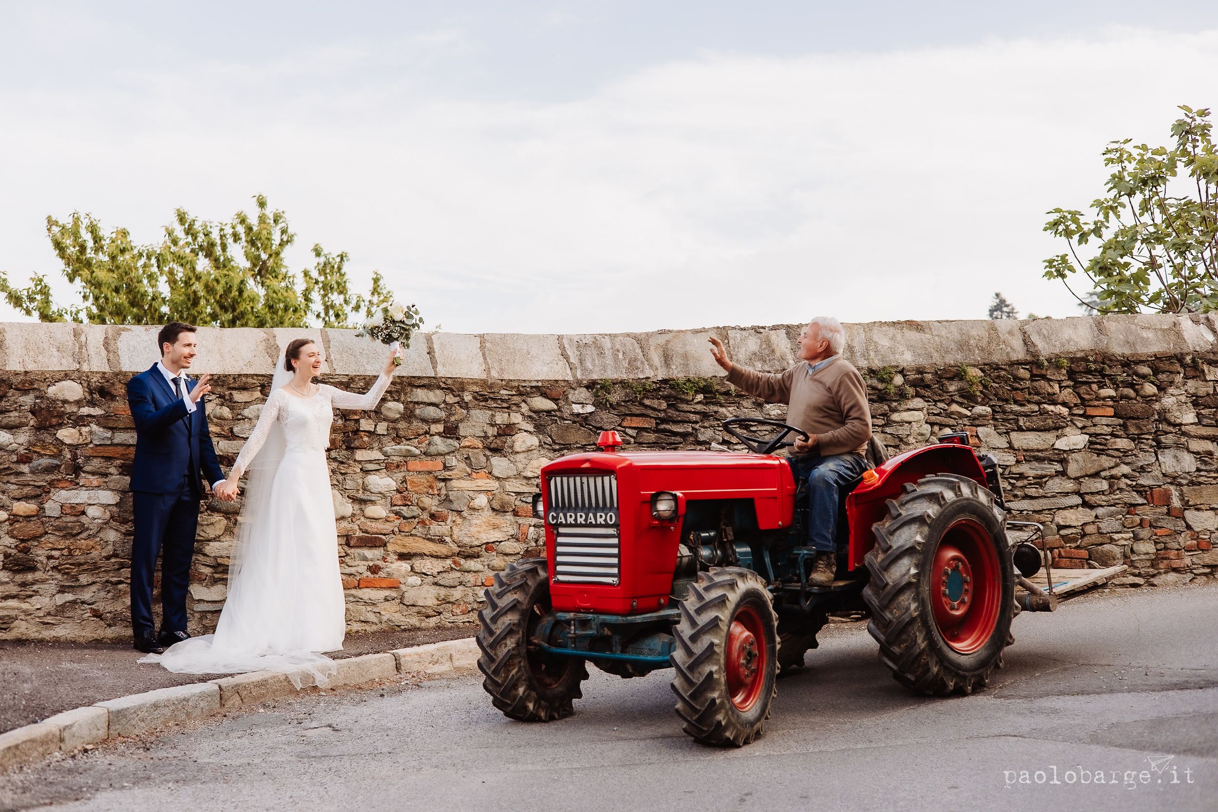 A vintage red tractor parked by a stone wall during wedding photos on an overcast day.