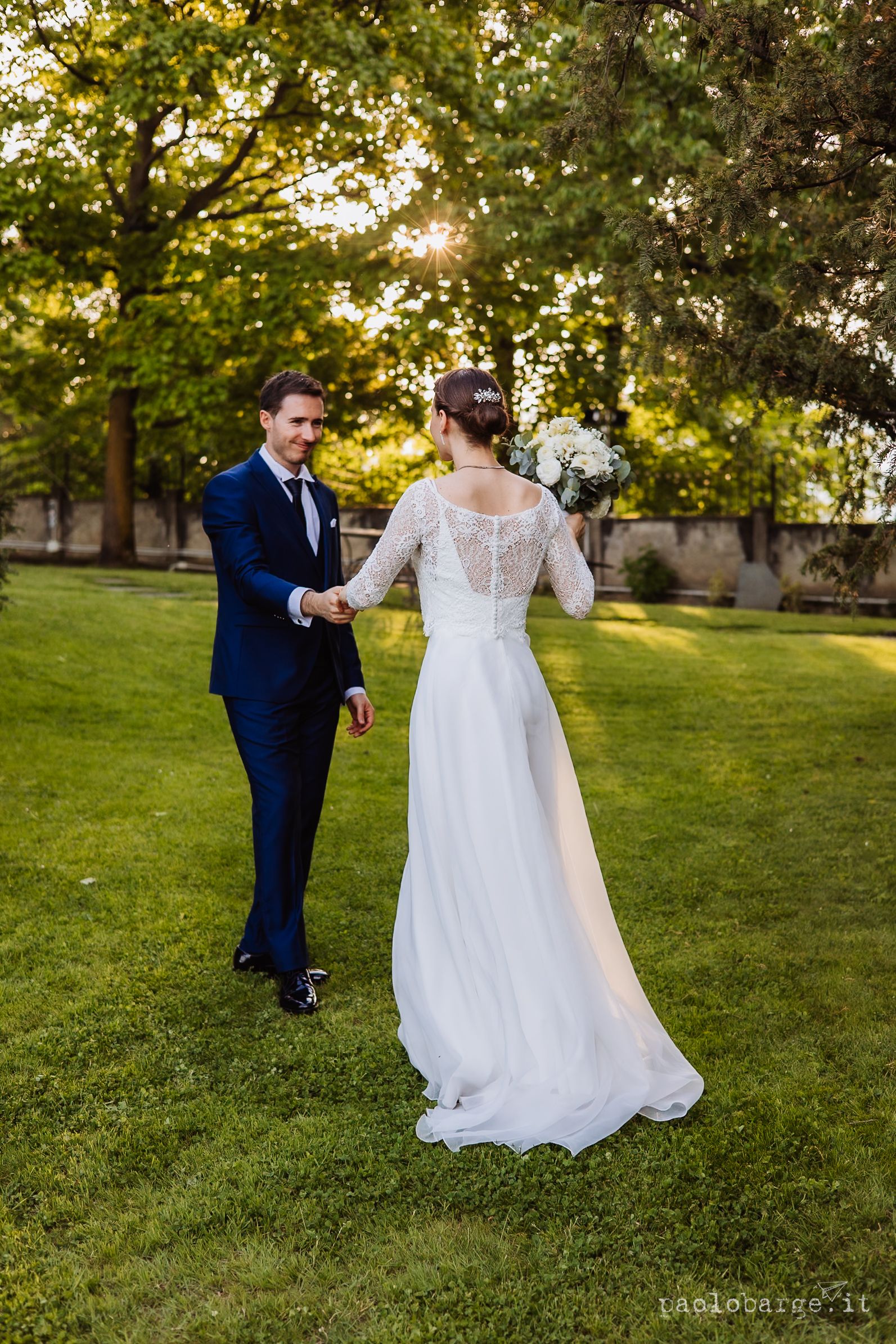 Couple dances together on a lush green lawn during golden hour at an outdoor wedding celebration.