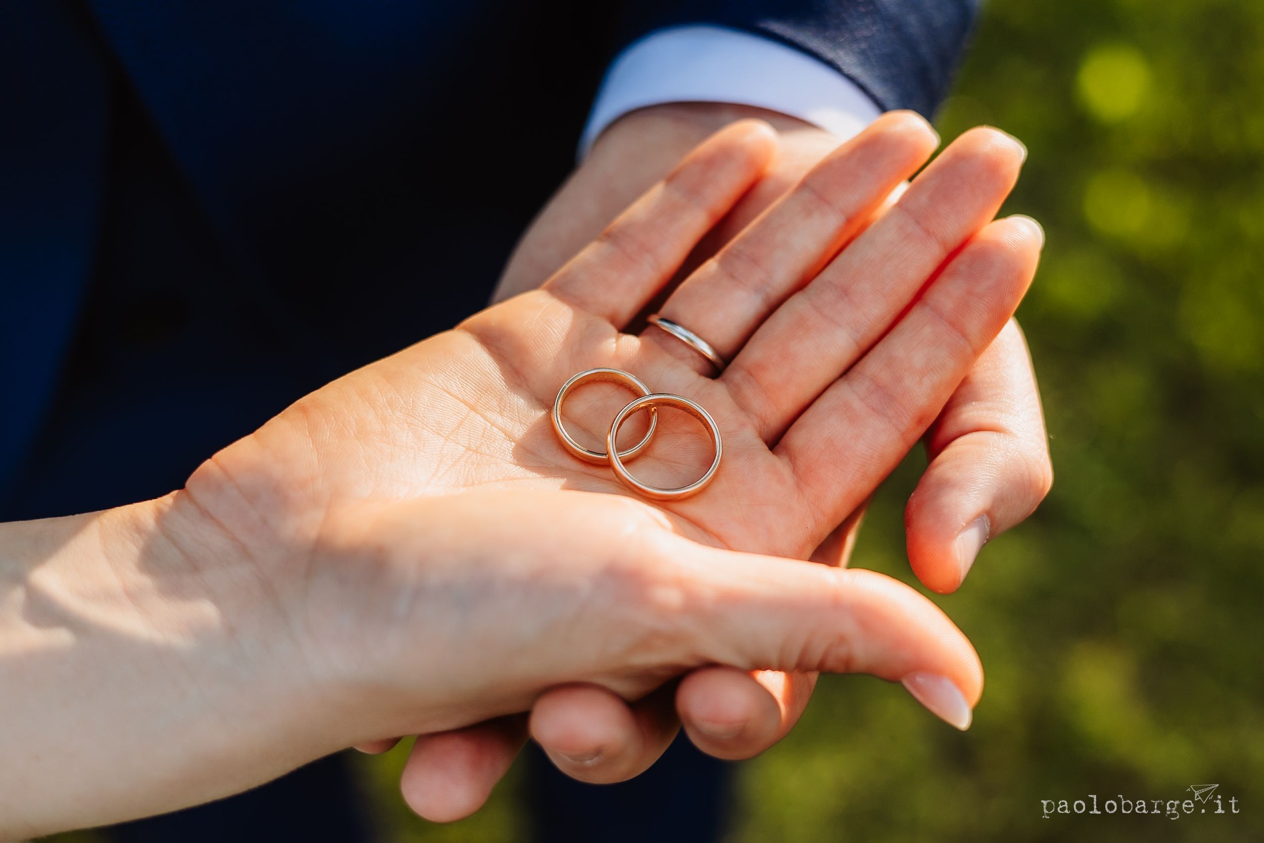 Two gold wedding rings rest in an open palm against a blurred green outdoor background.