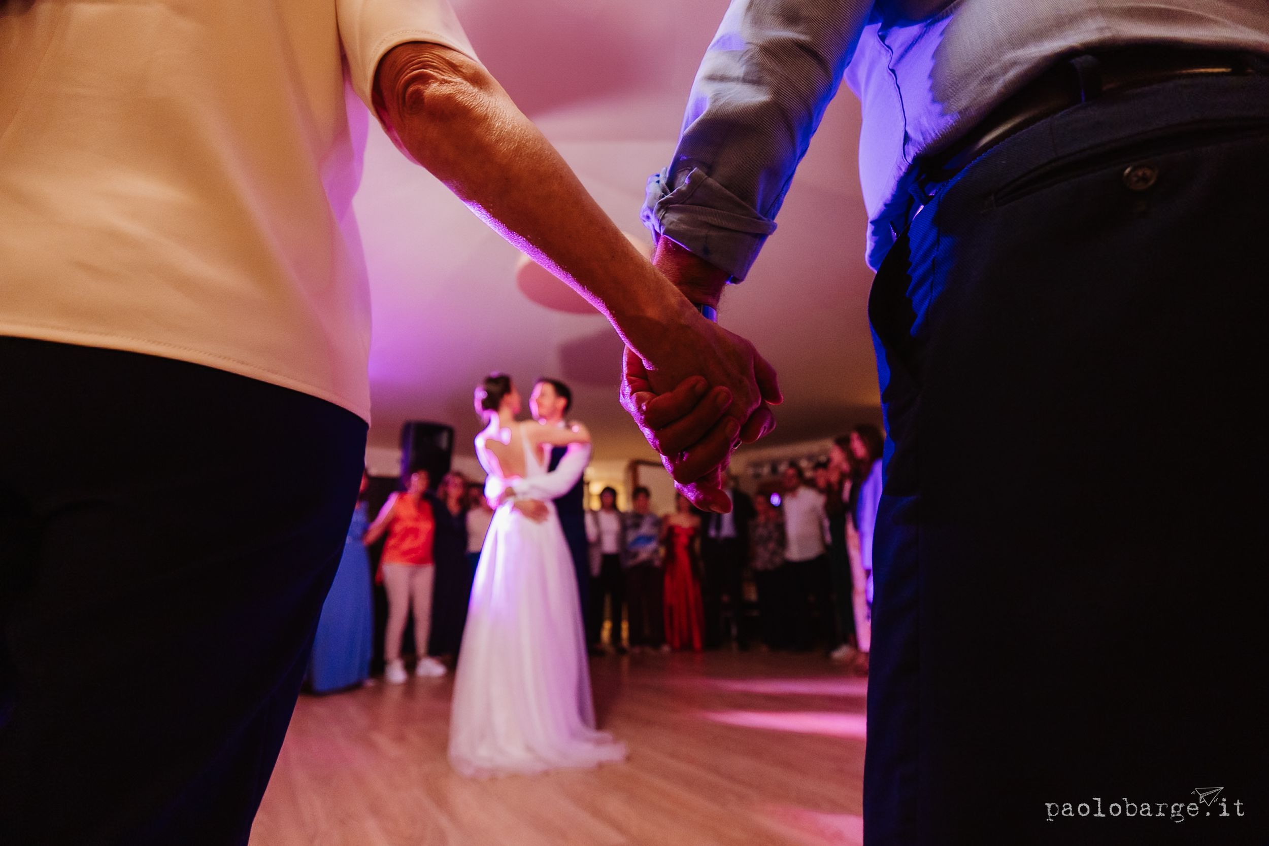 Wedding guests dance on a glowing pink-lit dance floor while others mingle at a reception celebration.
