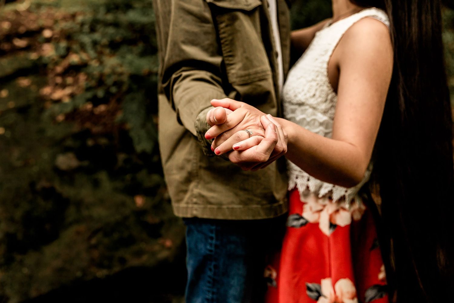 A romantic couple shares a tender moment against a green forest backdrop on an autumn day.