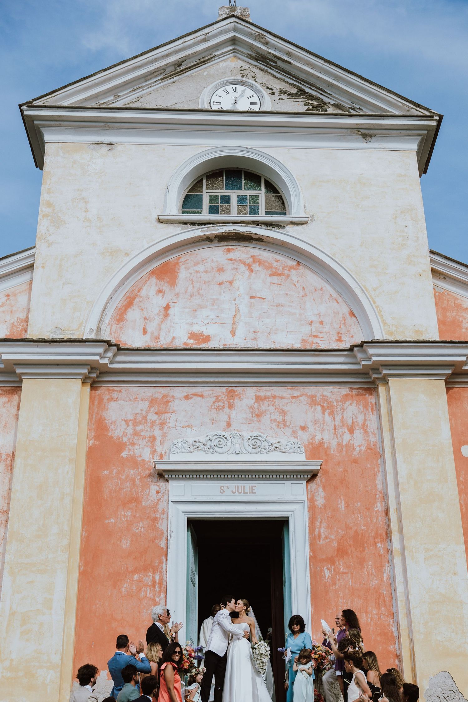 Wedding ceremony taking place at entrance of historic peach-colored church with arched doorway and classical architecture.