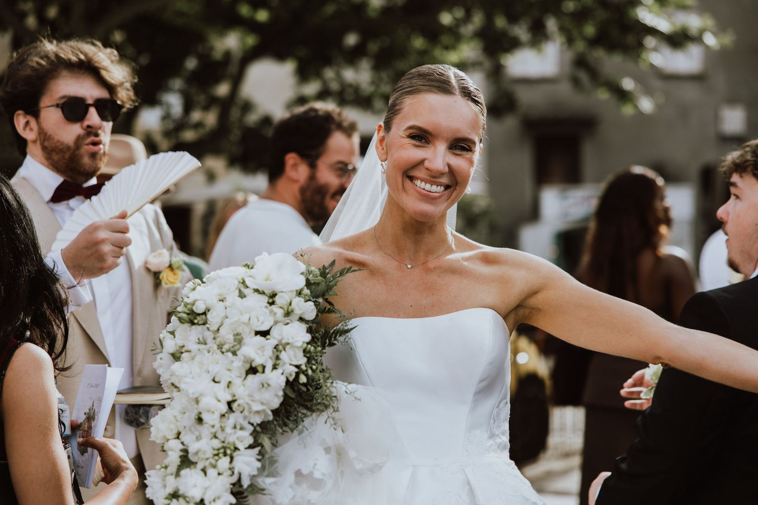 A wedding party celebrates with joyful laughter and white floral bouquets during an outdoor celebration.