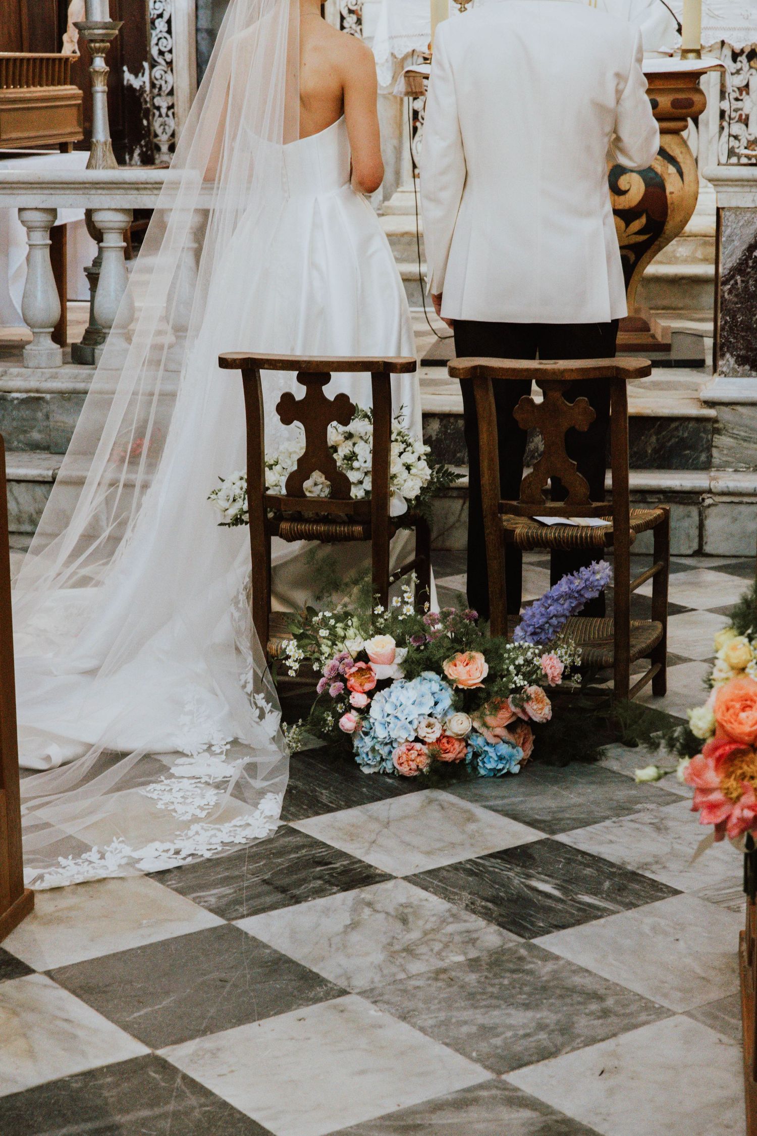 Two white wedding dresses and floral bouquets displayed on stone church steps during a ceremony.