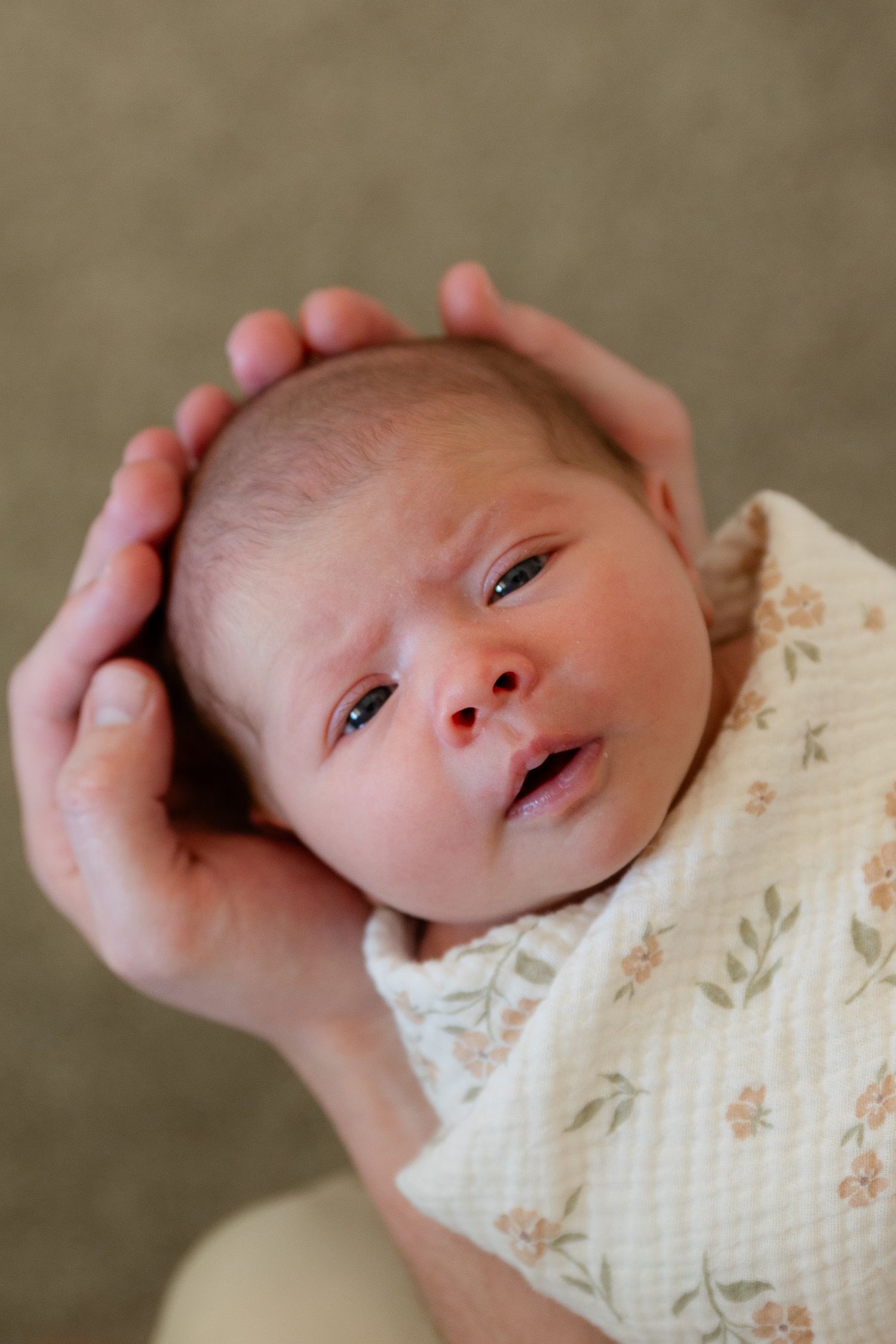 close of portrait of newborn baby with her eyes open. swaddles in a light colored flower blanket