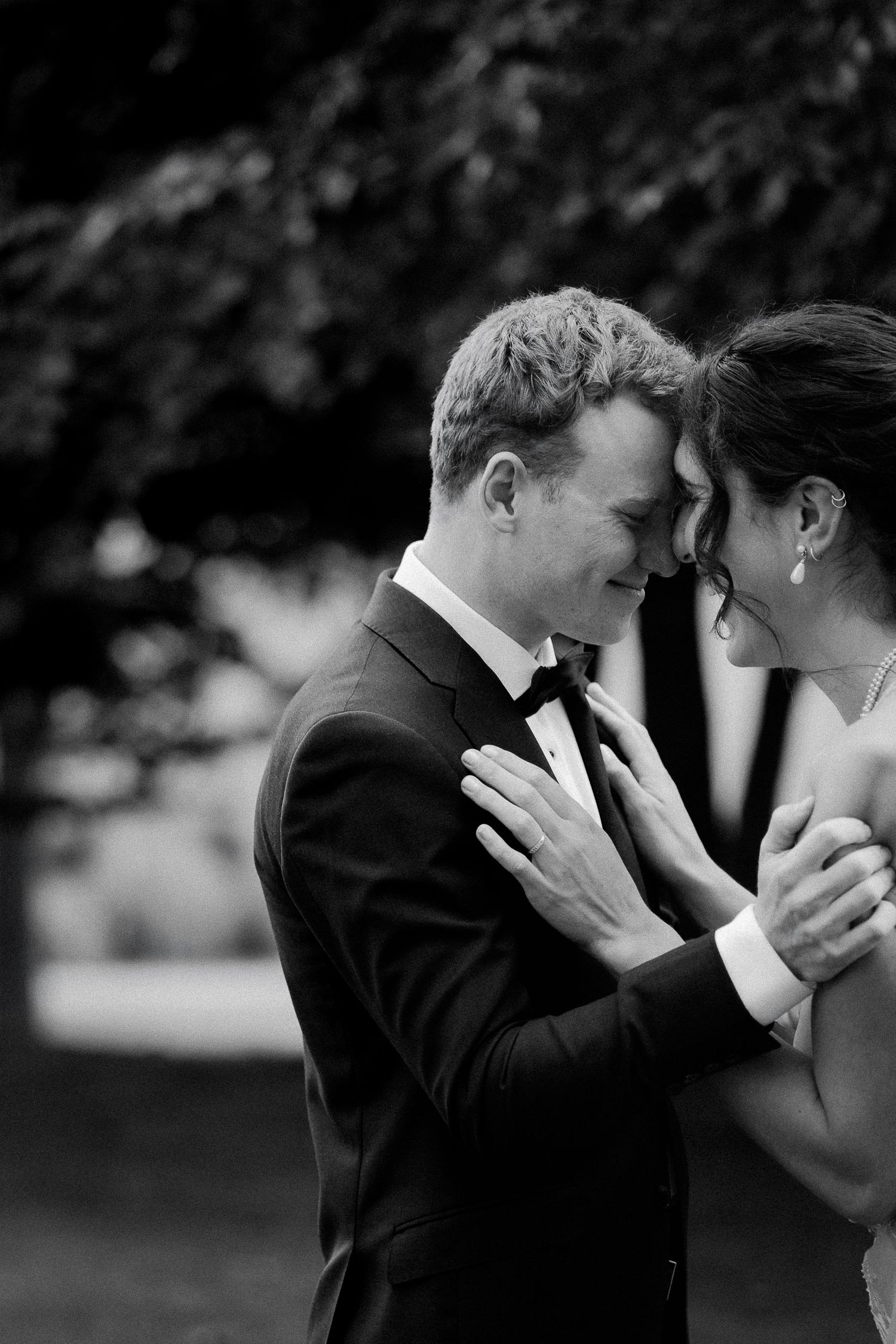 A tender black and white wedding moment captured as a couple shares an intimate embrace outdoors.