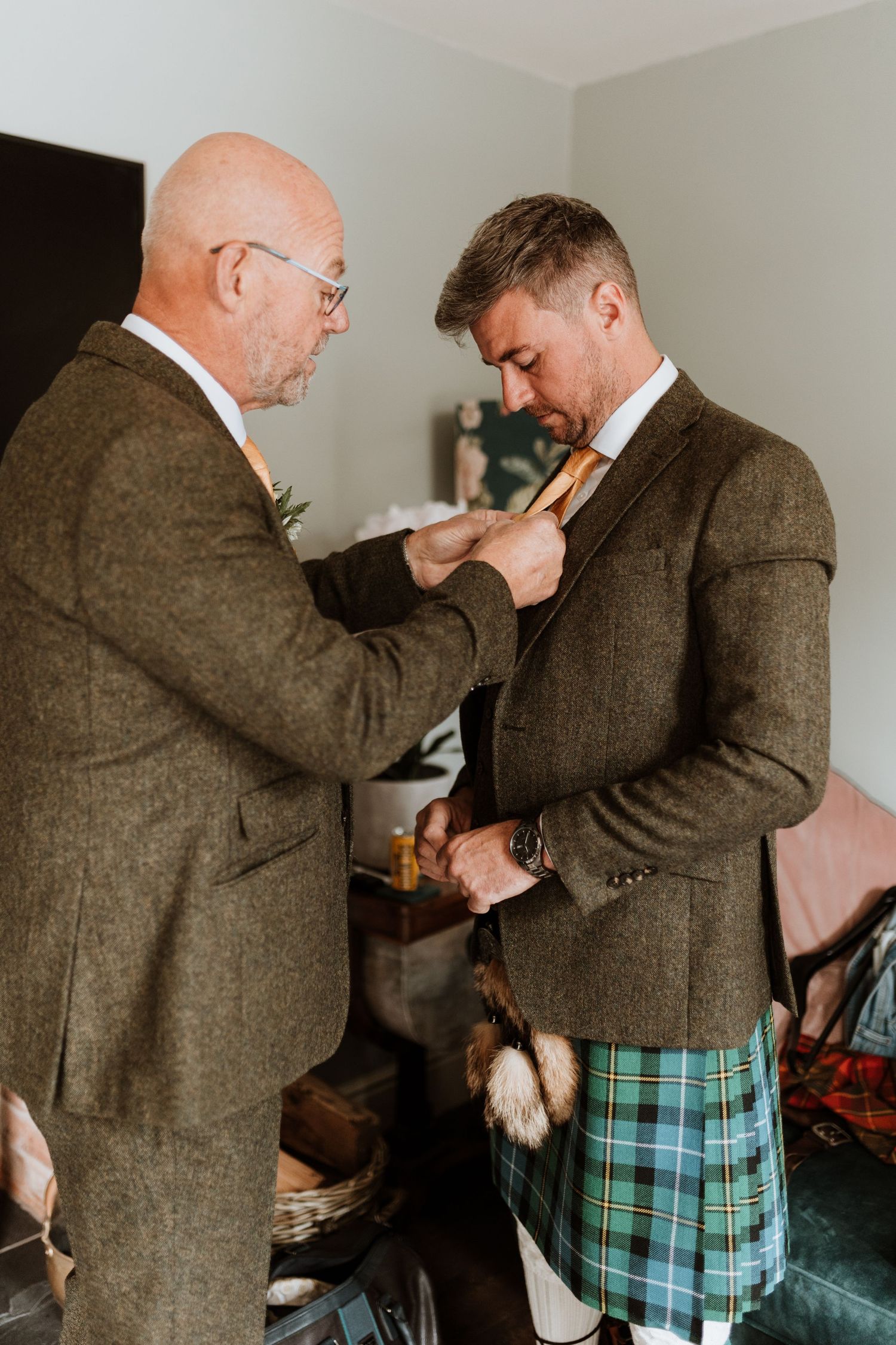 Person in traditional Scottish kilt adjusts jacket in sequence of getting dressed for formal occasion.