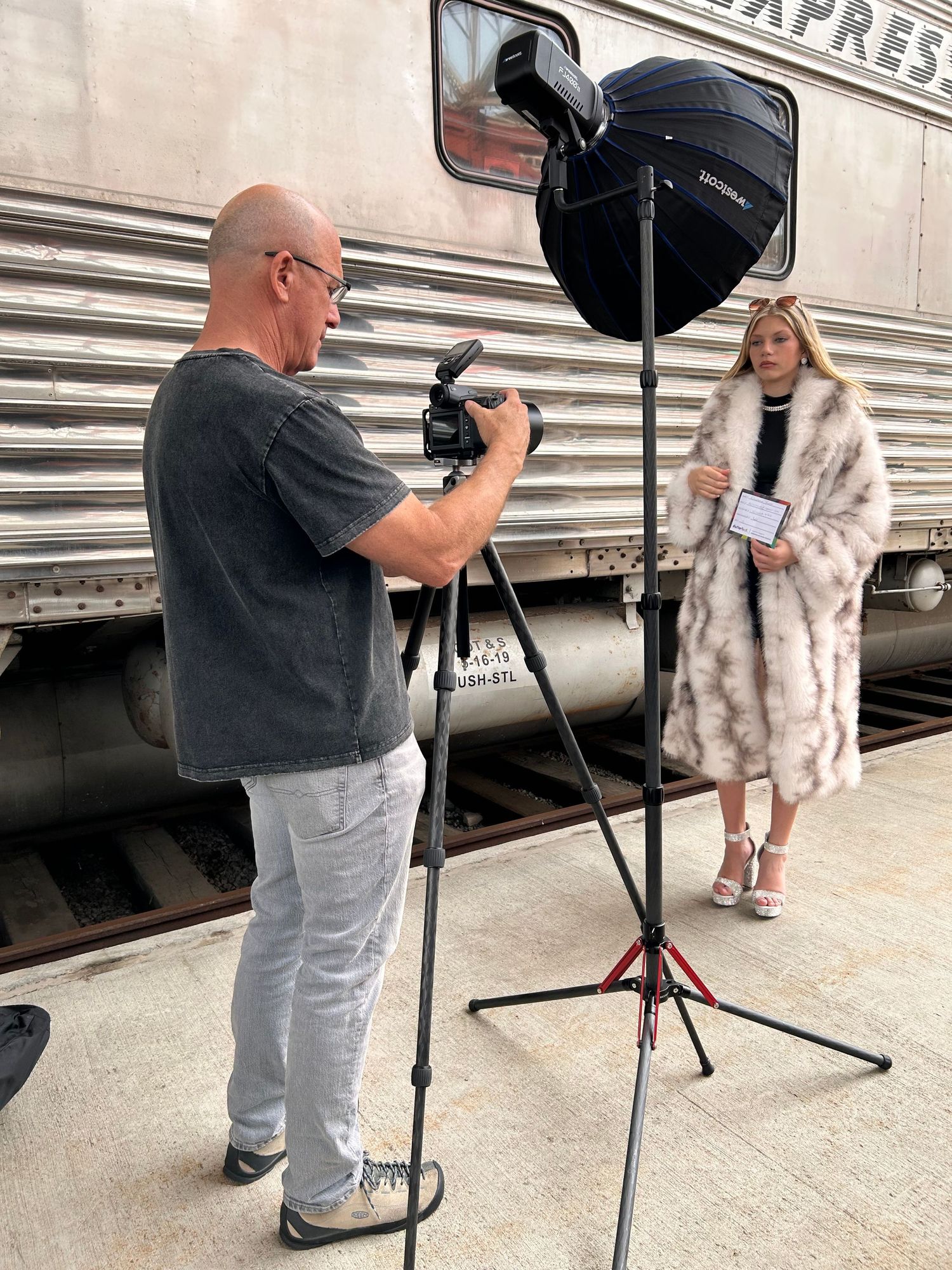 Professional photo shoot setup with lighting equipment and photographer next to a vintage train car.