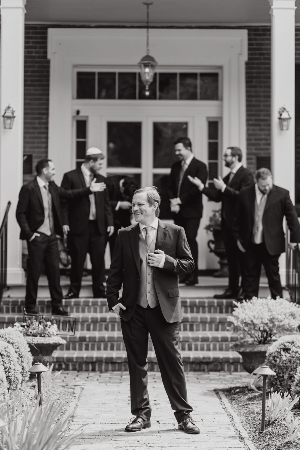Black and white photo of groomsmen in formal suits gathered outside a grand entrance with brick steps and white columns.