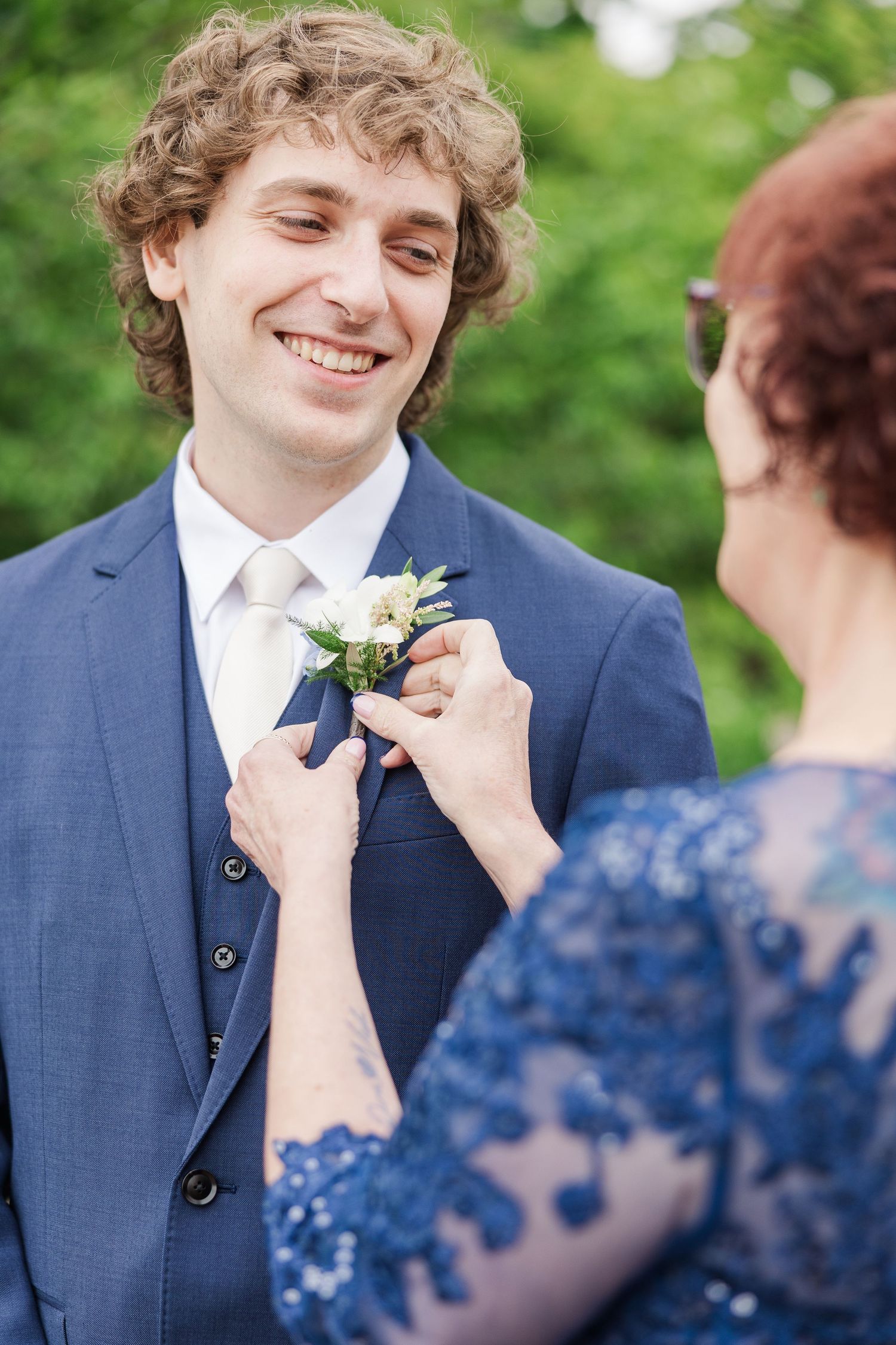 A person in a navy suit stands with someone wearing a sparkly blue formal dress and glasses at a special event.