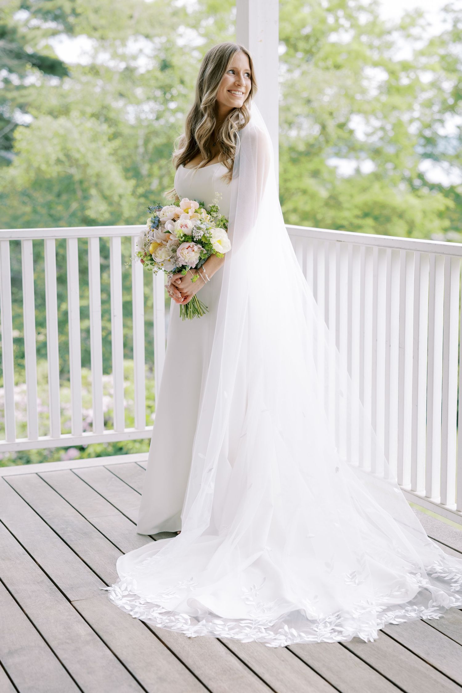 White dress hangs on exterior wall of gray house with rocking chairs on rustic front porch.