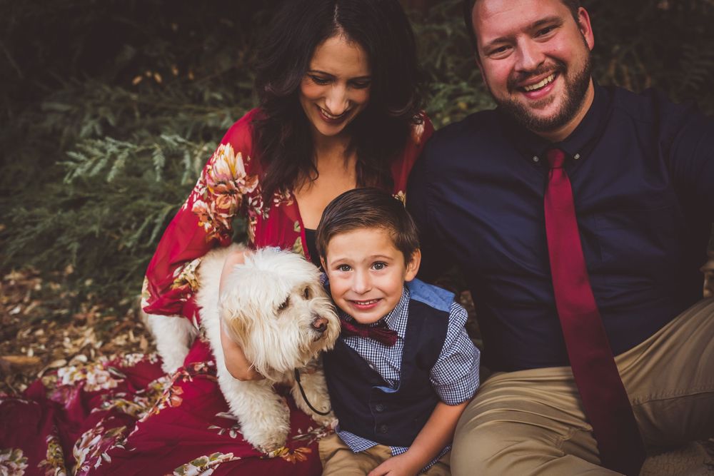 Family sitting outdoors with their fluffy white dog during a fall portrait session in coordinated formal attire.