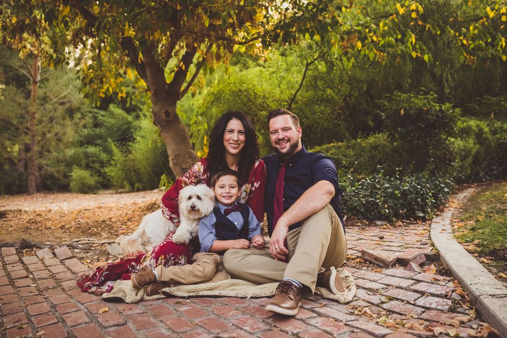 A family and their beloved dog pose together outdoors on a sunny autumn day for a heartwarming photo session.