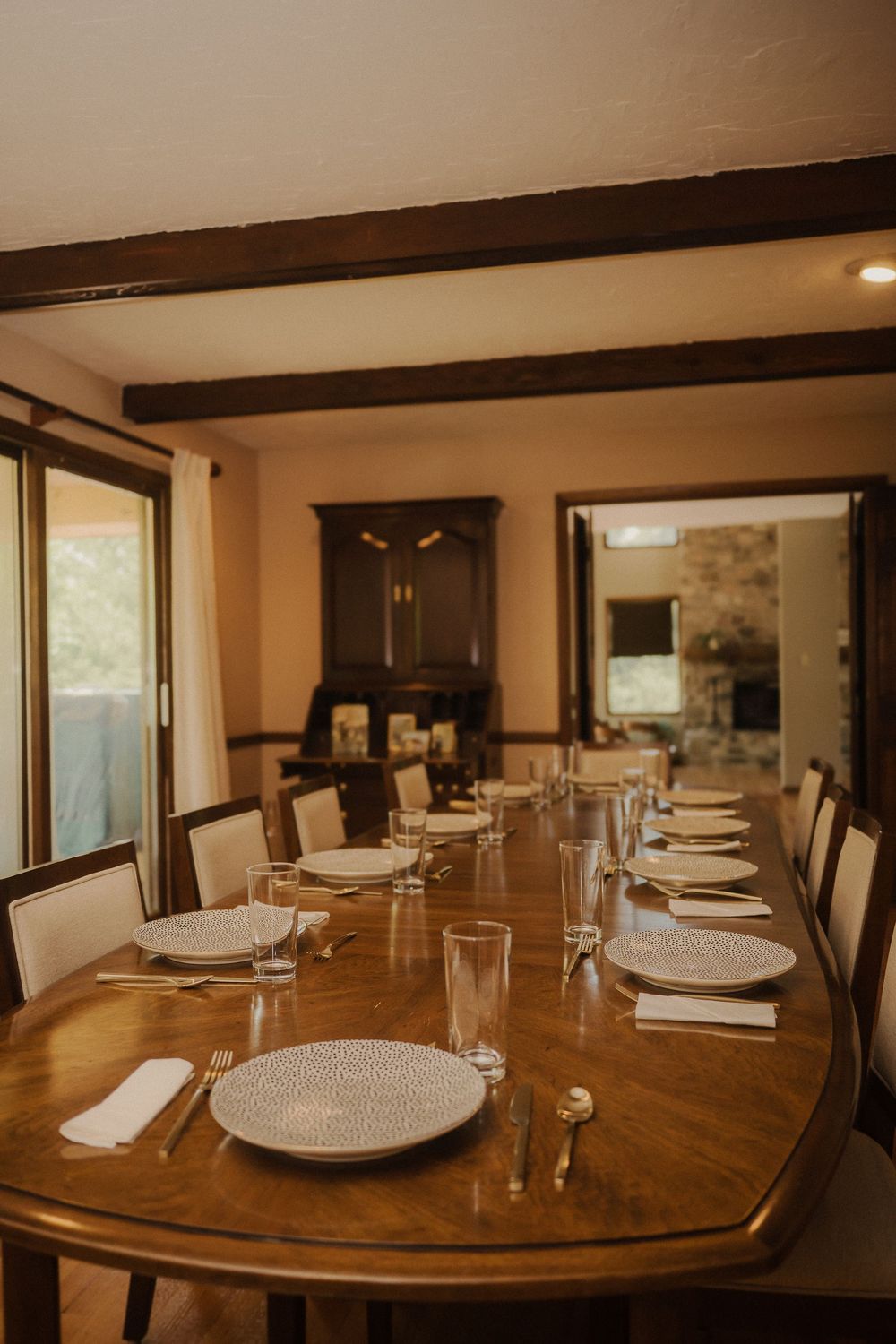 Elegant dining table set for dinner service with white plates and rustic wooden beams in warm lighting.