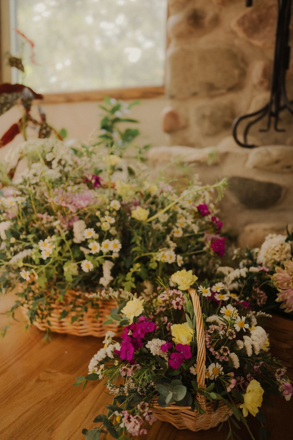 Woven baskets filled with colorful garden flowers create a rustic wedding centerpiece arrangement on wooden tables.