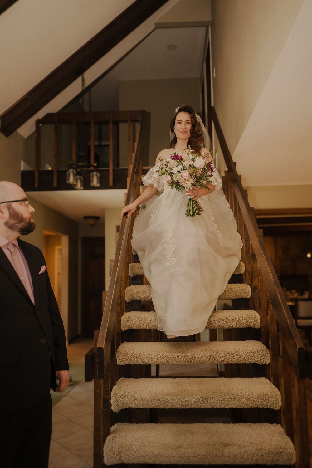 Elegant bridal gown detail as person walks up stone staircase in rustic indoor setting with wooden beams.