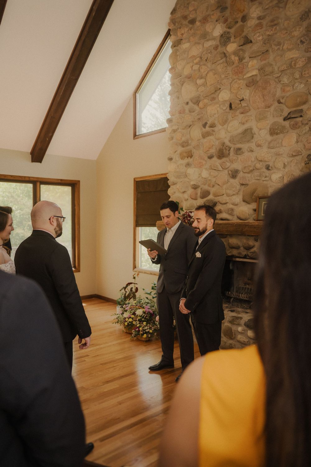 Wedding ceremony in rustic room with stone firewall, wooden beams, and hardwood floors.