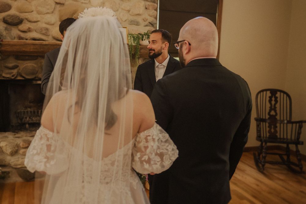 A wedding ceremony takes place in a rustic room with stone walls and wooden floors during an intimate indoor service.
