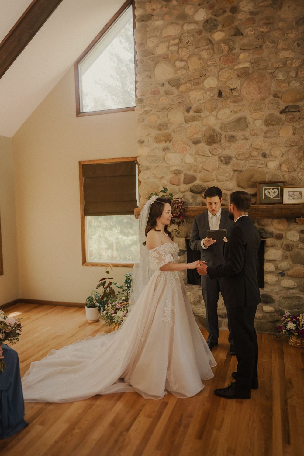 An intimate wedding ceremony in front of a floor-to-ceiling stone fireplace in a rustic venue with hardwood floors.