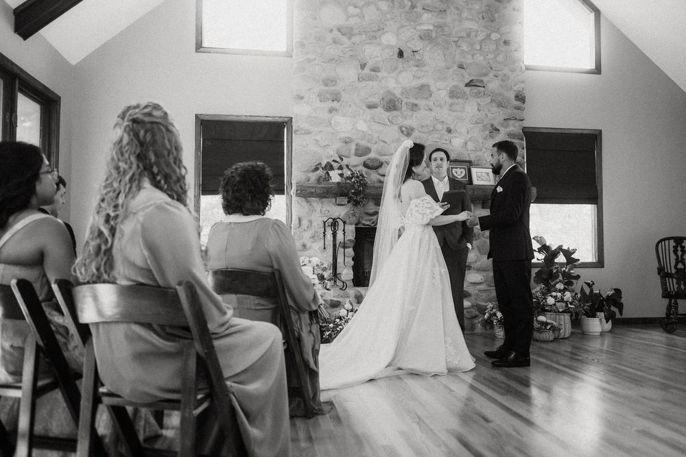 Black and white photograph of a wedding ceremony taking place in a rustic indoor venue with stone walls.