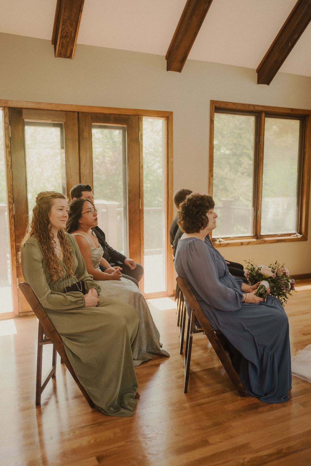 People sitting against a wall in a rustic room with wooden floors and beams in matching muted dresses.