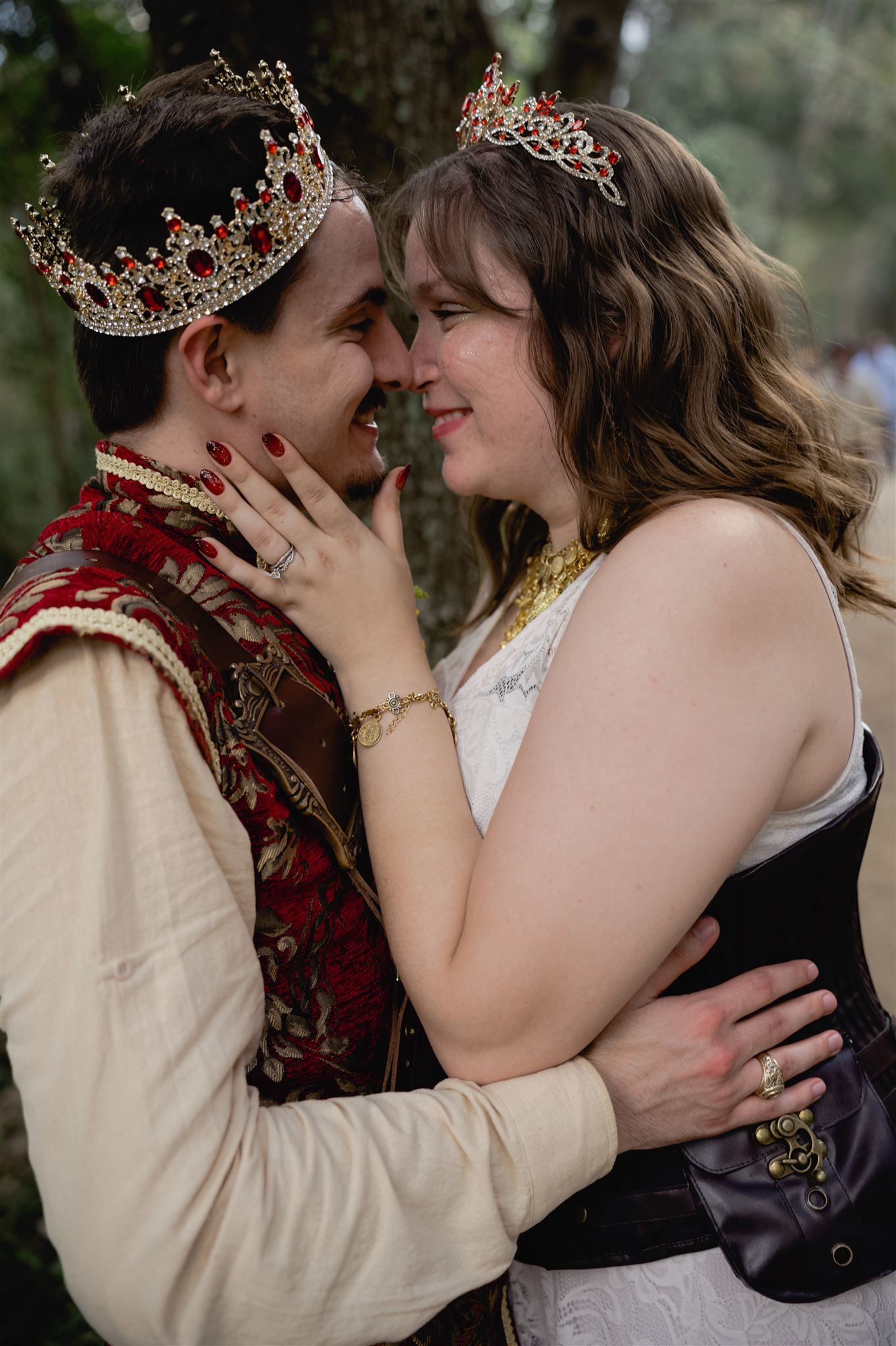 A couple in medieval renaissance costumes with matching crowns share an intimate moment during a themed photoshoot.