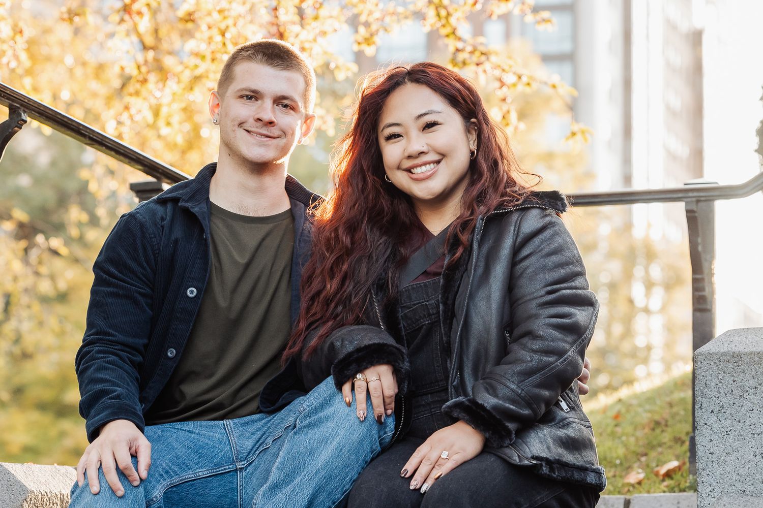 Couple sitting together on stone steps during fall with golden foliage in background.