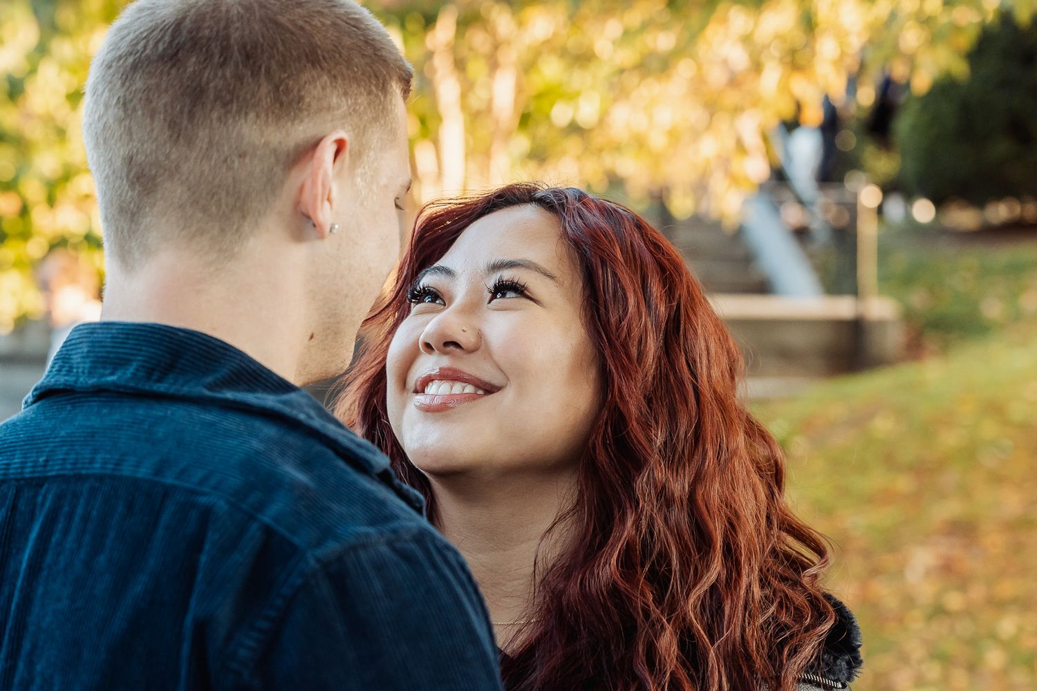 Intimate moment between couple with golden autumn trees and bridge in background.