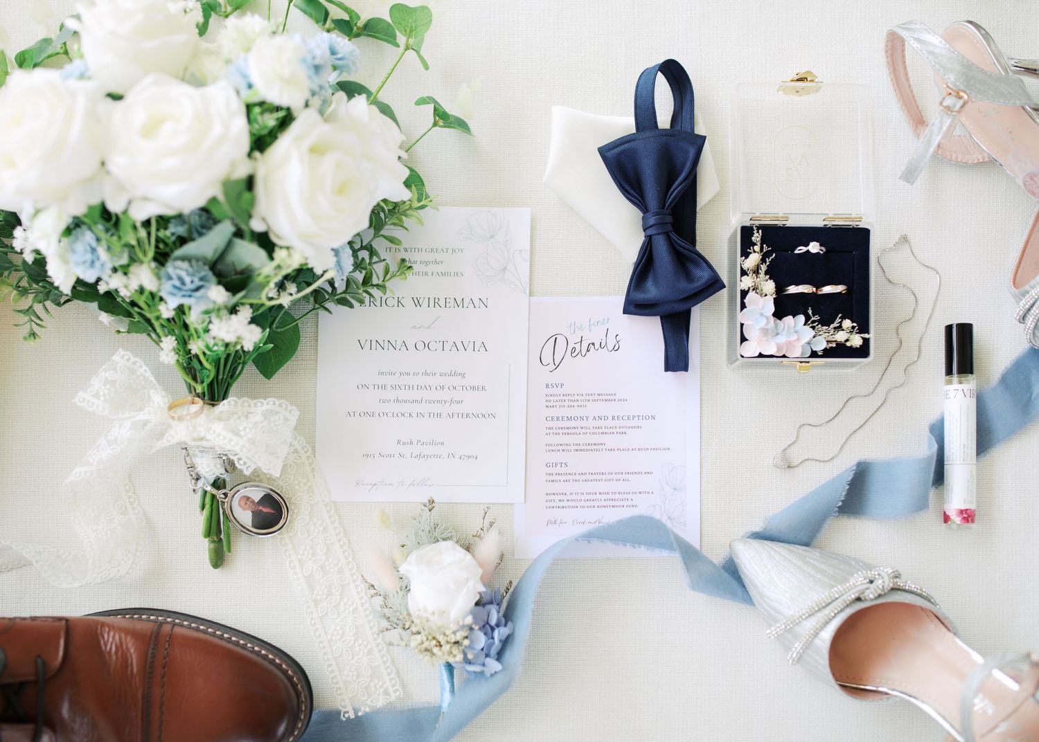 Wedding stationery flatlay with navy bow tie, florals and invitation suite.