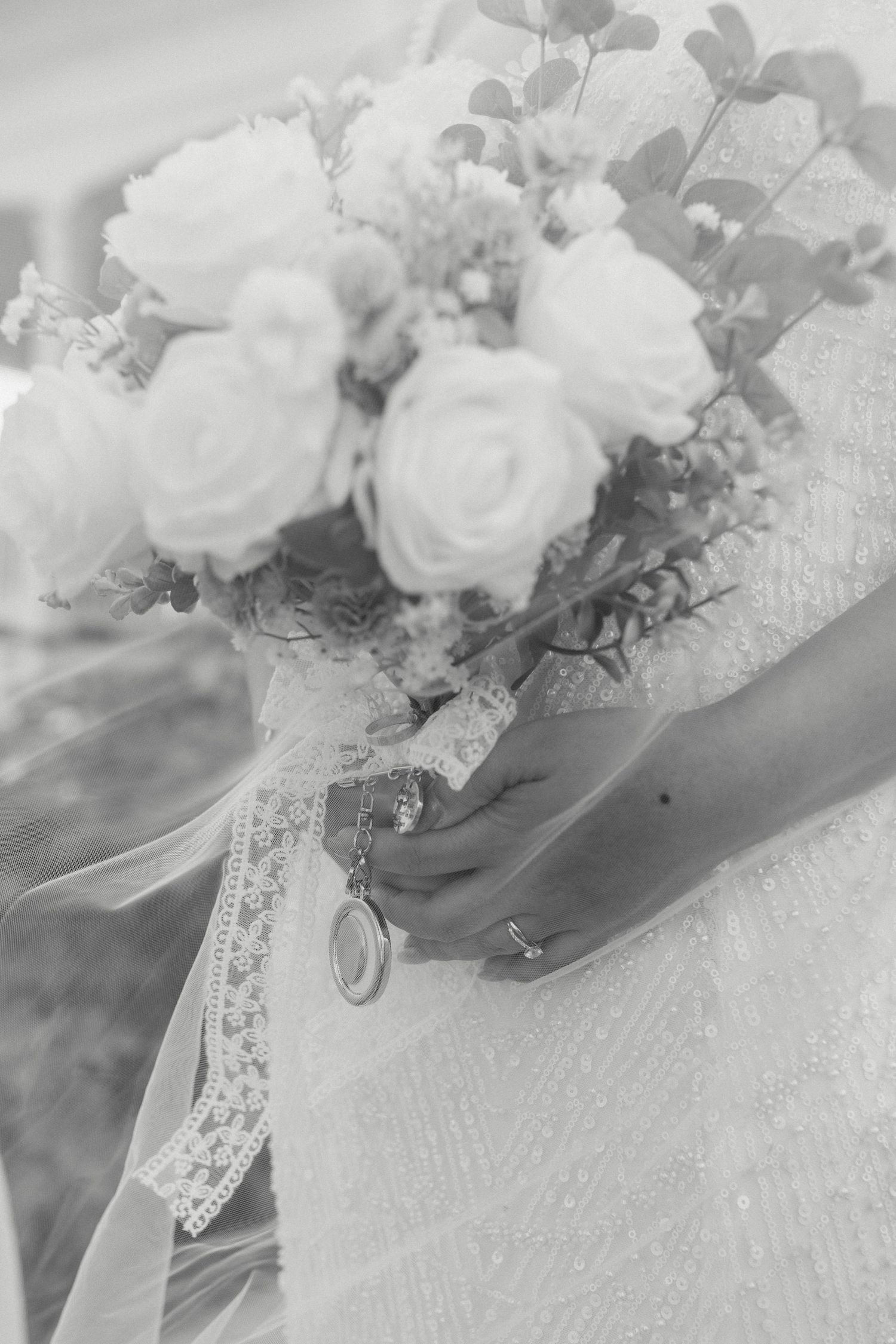 Elegant white wedding bouquet with roses and delicate lace ribbon in a soft black and white photograph.