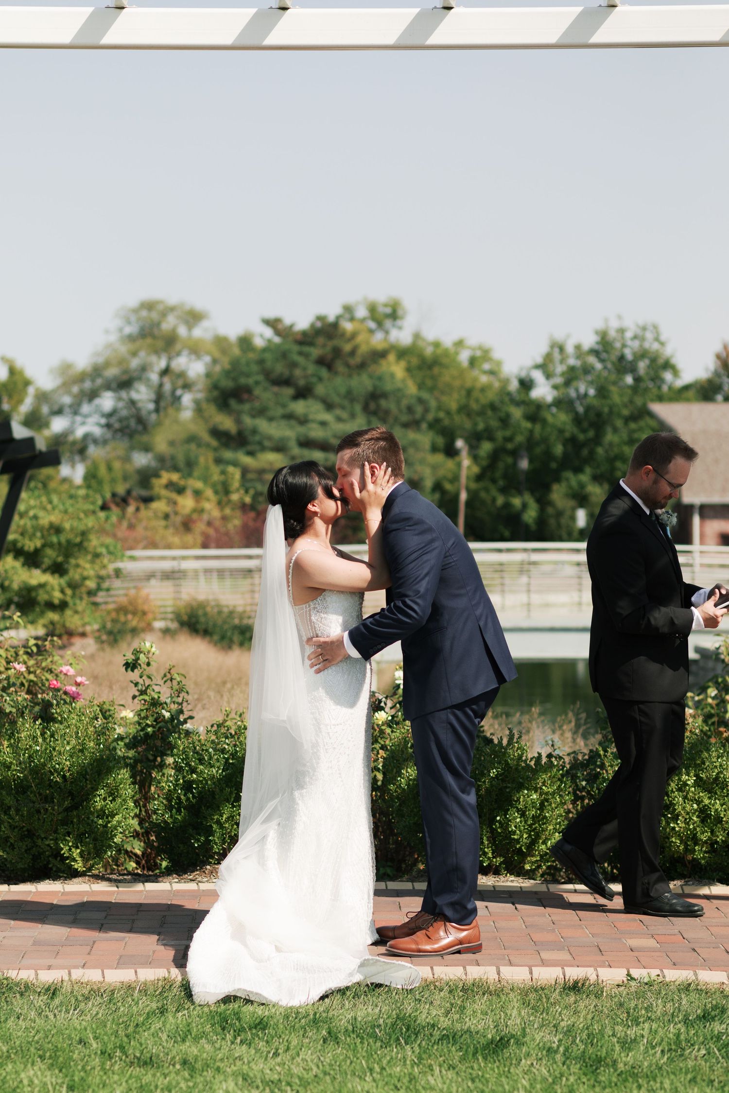 Wedding ceremony taking place on a brick patio under a white pergola on a sunny day.