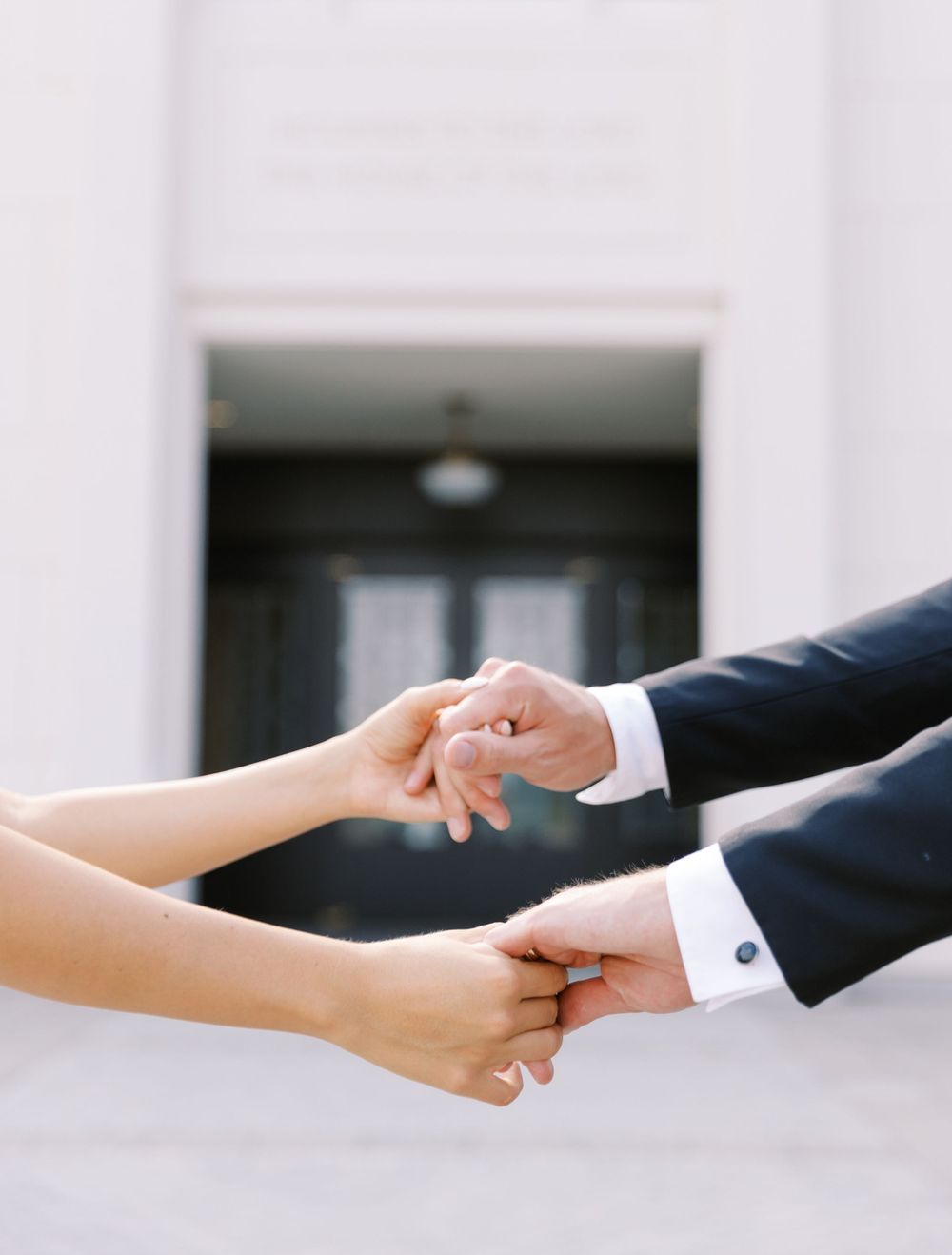Two hands reaching to hold each other tenderly in an intimate moment against a white building backdrop.