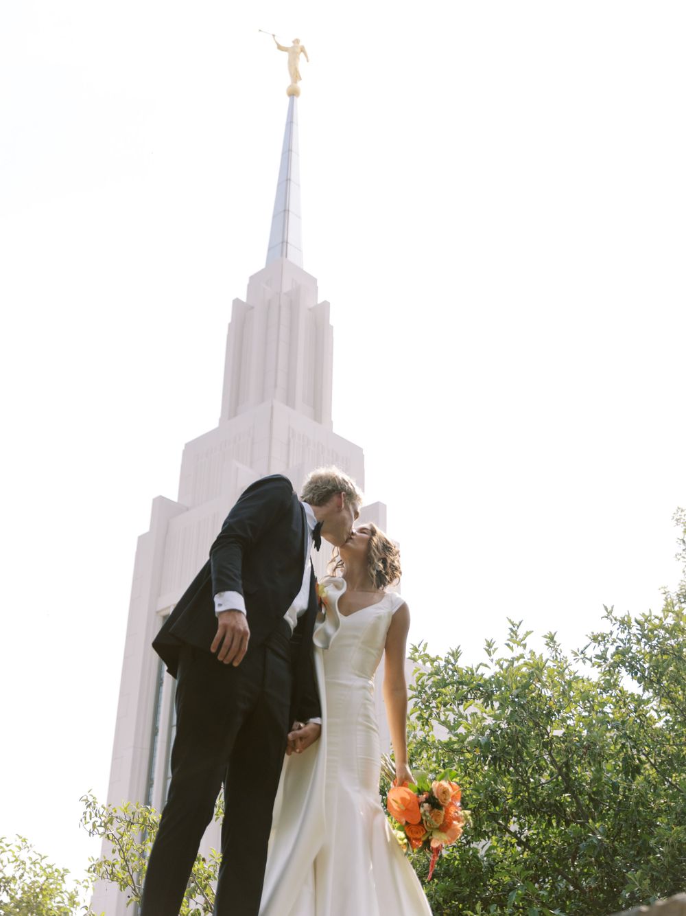 Newlywed couple embraces in front of a LDS temple spire during a sunset wedding photoshoot.