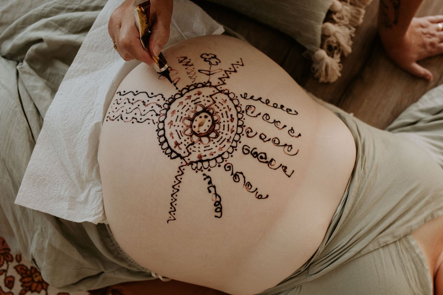 A close-up view of a henna tattoo design featuring a circular sun pattern on a pregnant woman's belly.