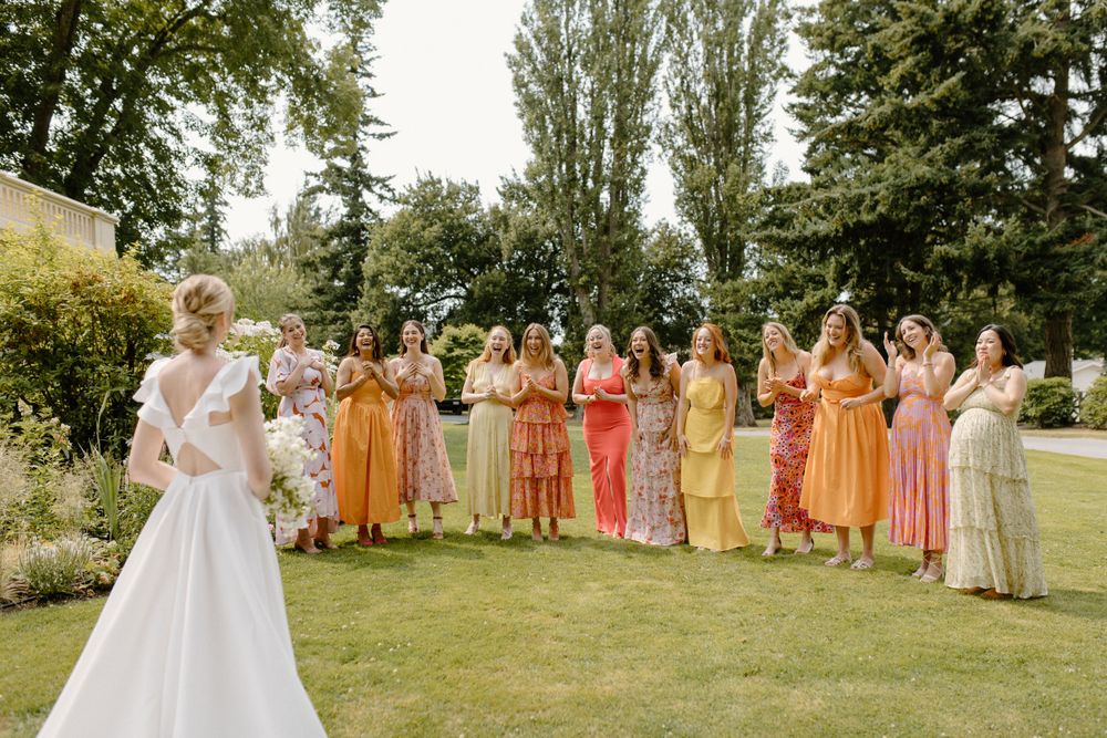 Wedding party with attendants in sunset-hued dresses standing on a lush garden lawn during summer festivities.