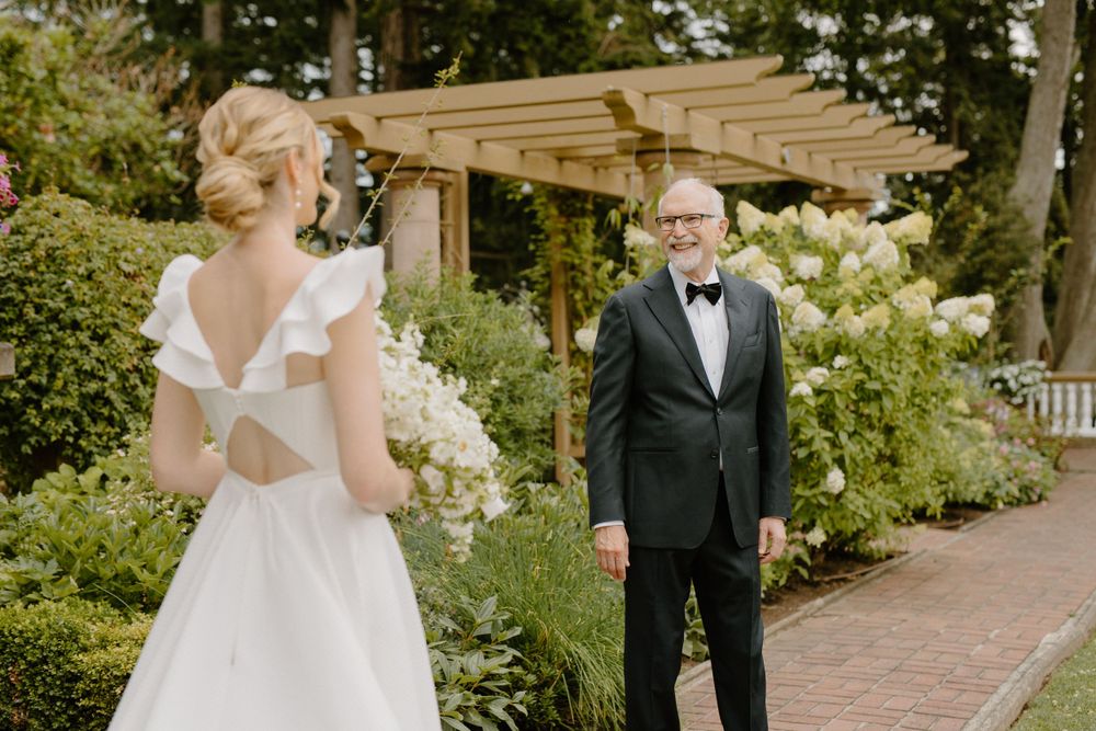 A first look wedding moment between a bride in a white dress and groom in a tuxedo in a garden setting.