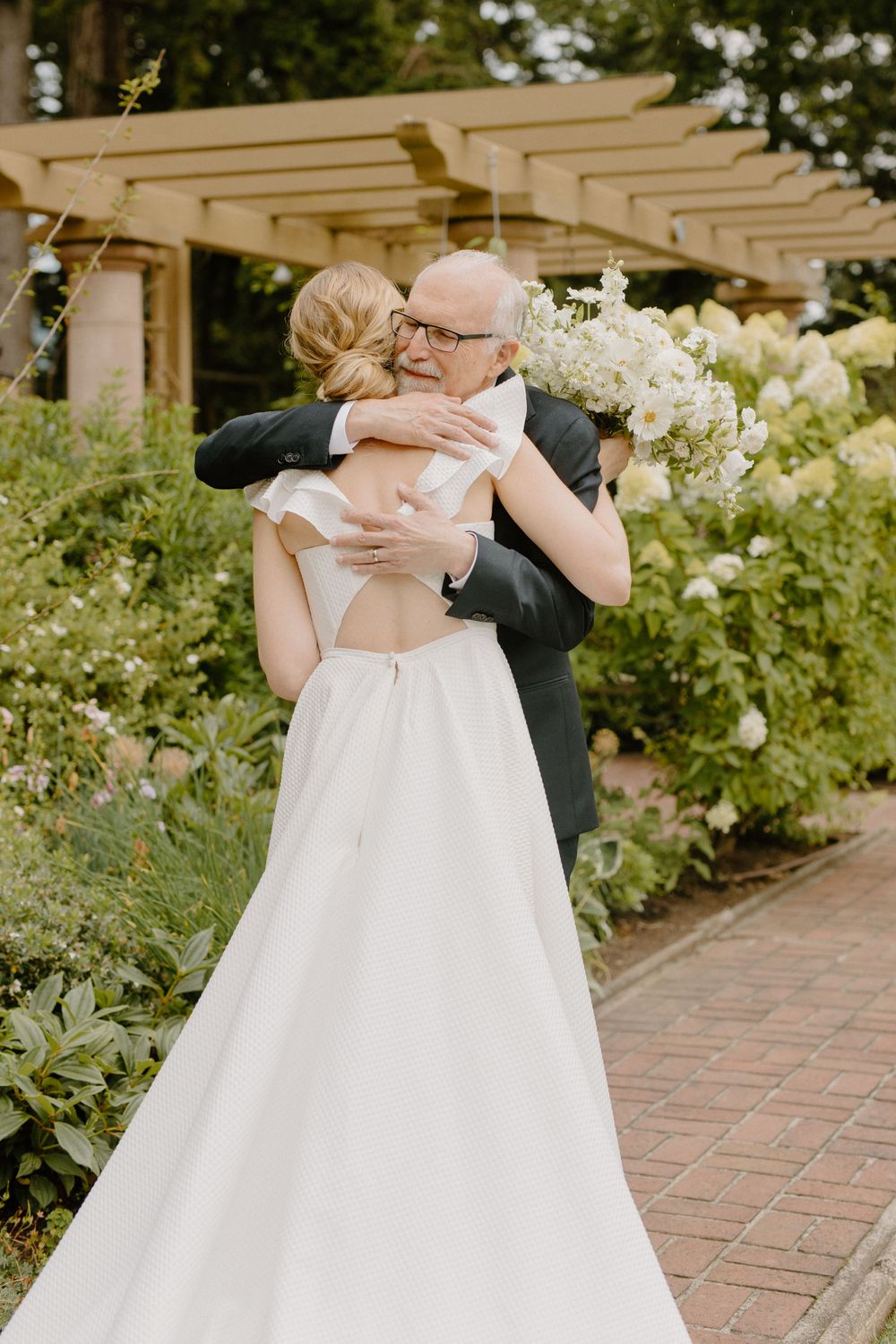 A heartfelt embrace between two people at a garden wedding venue with a white gown and floral bouquet.