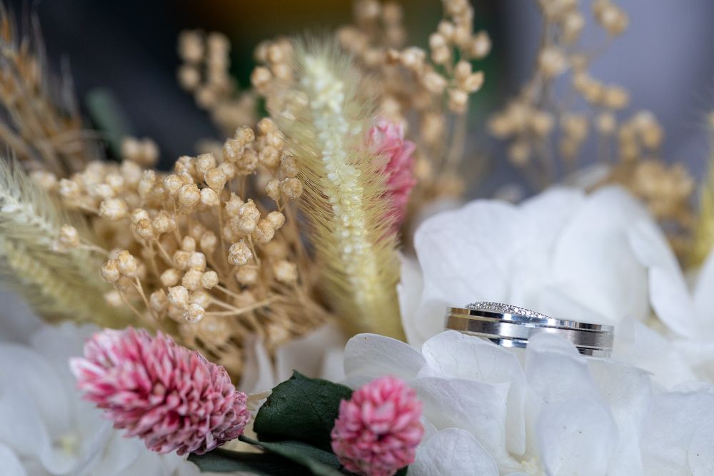 Macro shot of wedding rings nestled among white and pink floral decorations.