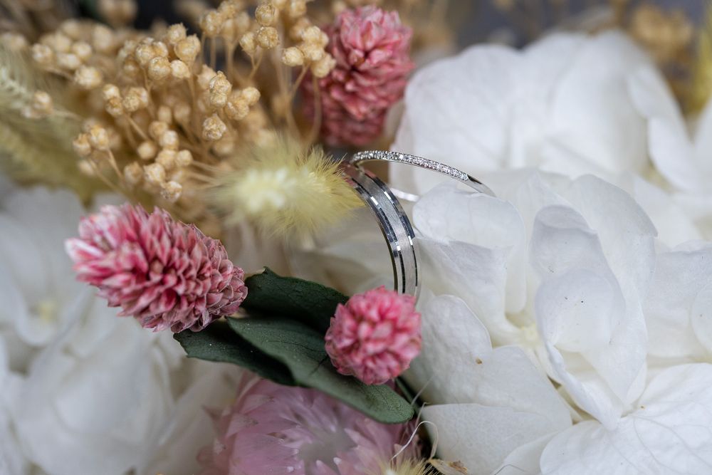 Detailed view of wedding bands surrounded by delicate white petals and pink blooms.