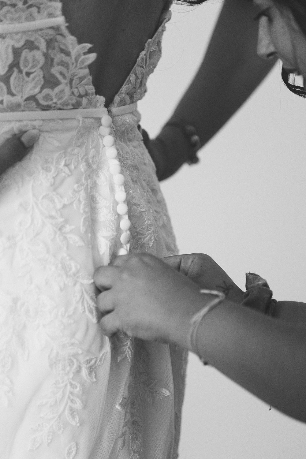 Close-up of hands buttoning up intricate lace details on wedding gown.