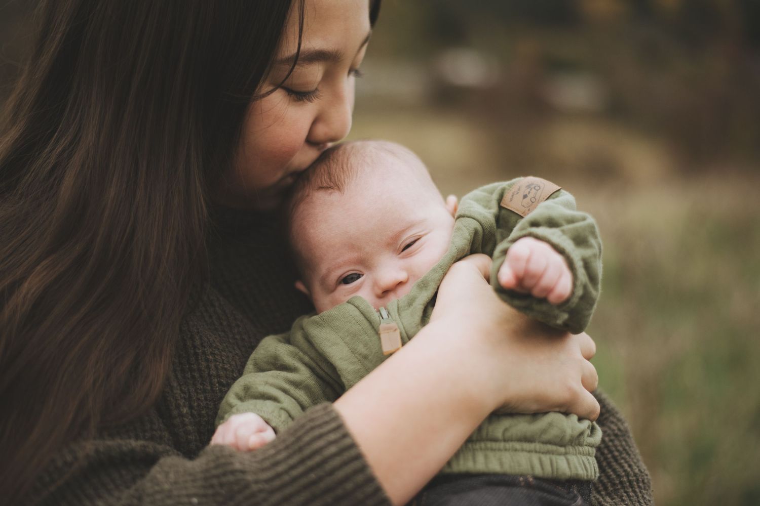 A tender moment between a sister and baby in green jacket as they embrace outdoors in soft natural light.