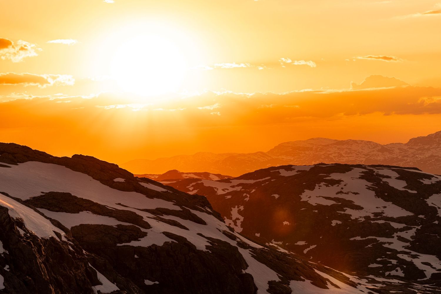 Spectacular orange sunset illuminates snow-covered mountain peaks with vibrant warm colors across a rugged landscape. folgefonna sommer ski