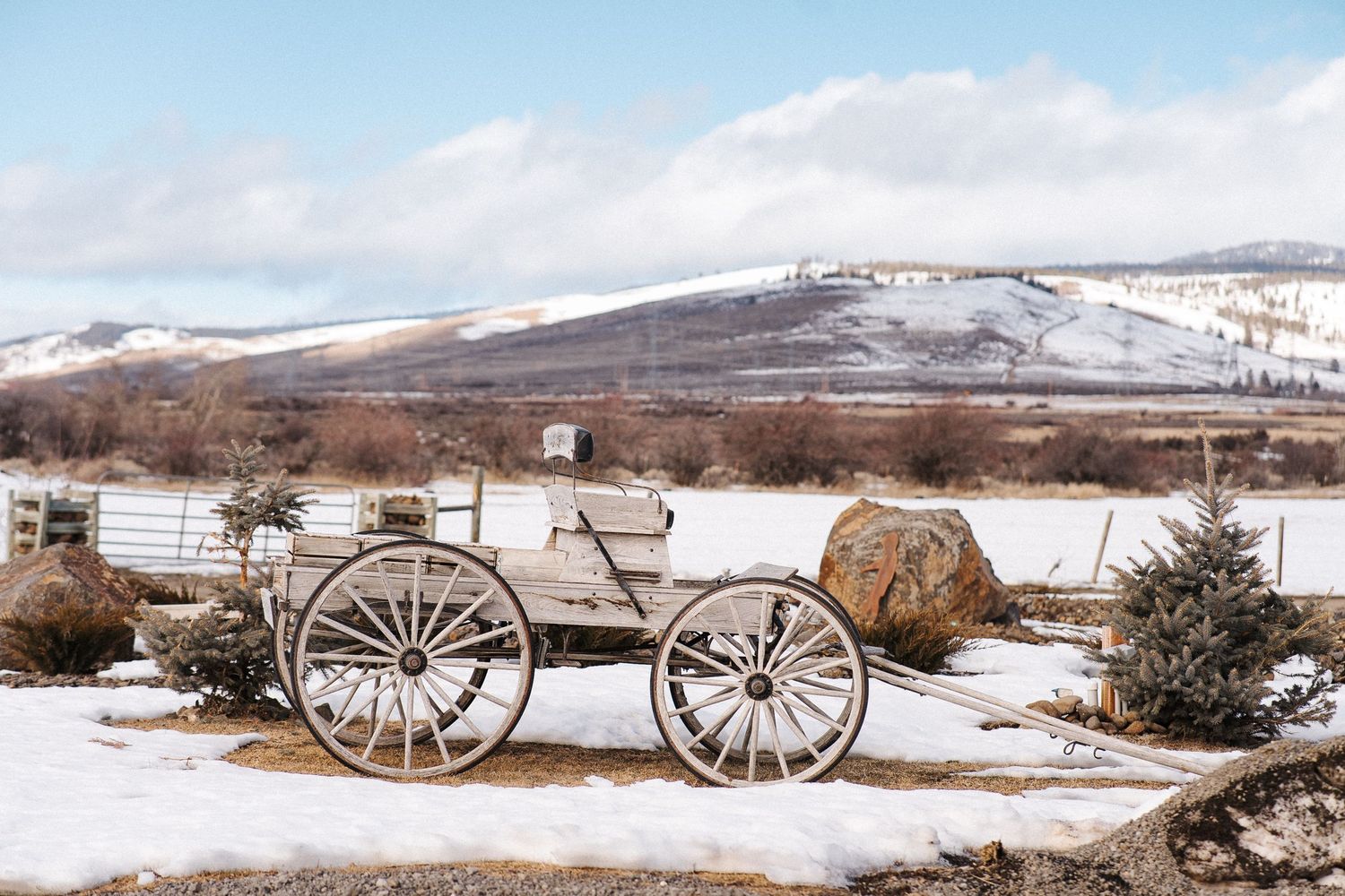 A snowy winter landscape with wooden fence stretching along a rural field under dramatic cloudy skies.