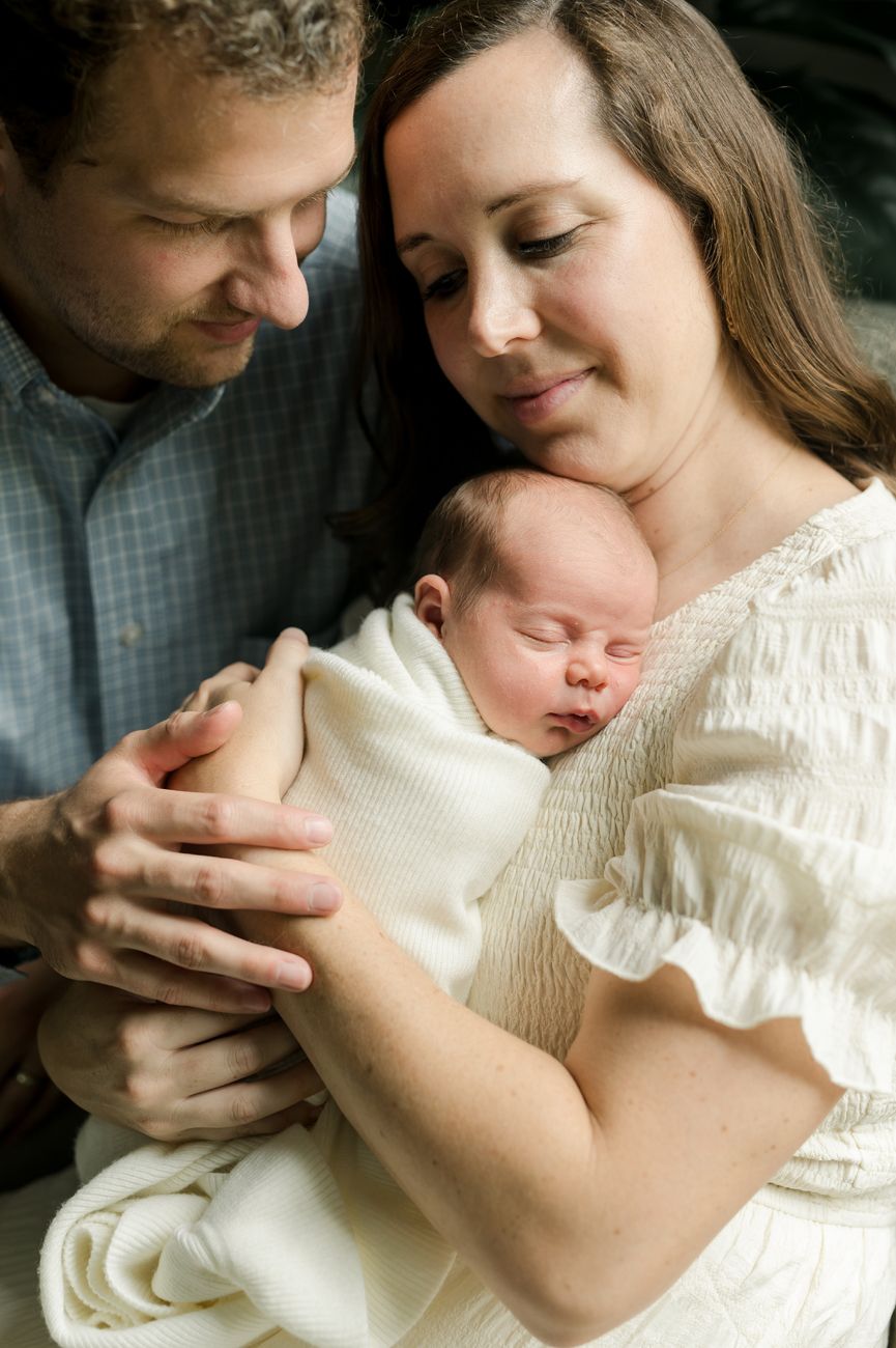 A tender moment as parents cradle their newborn baby wrapped in white.