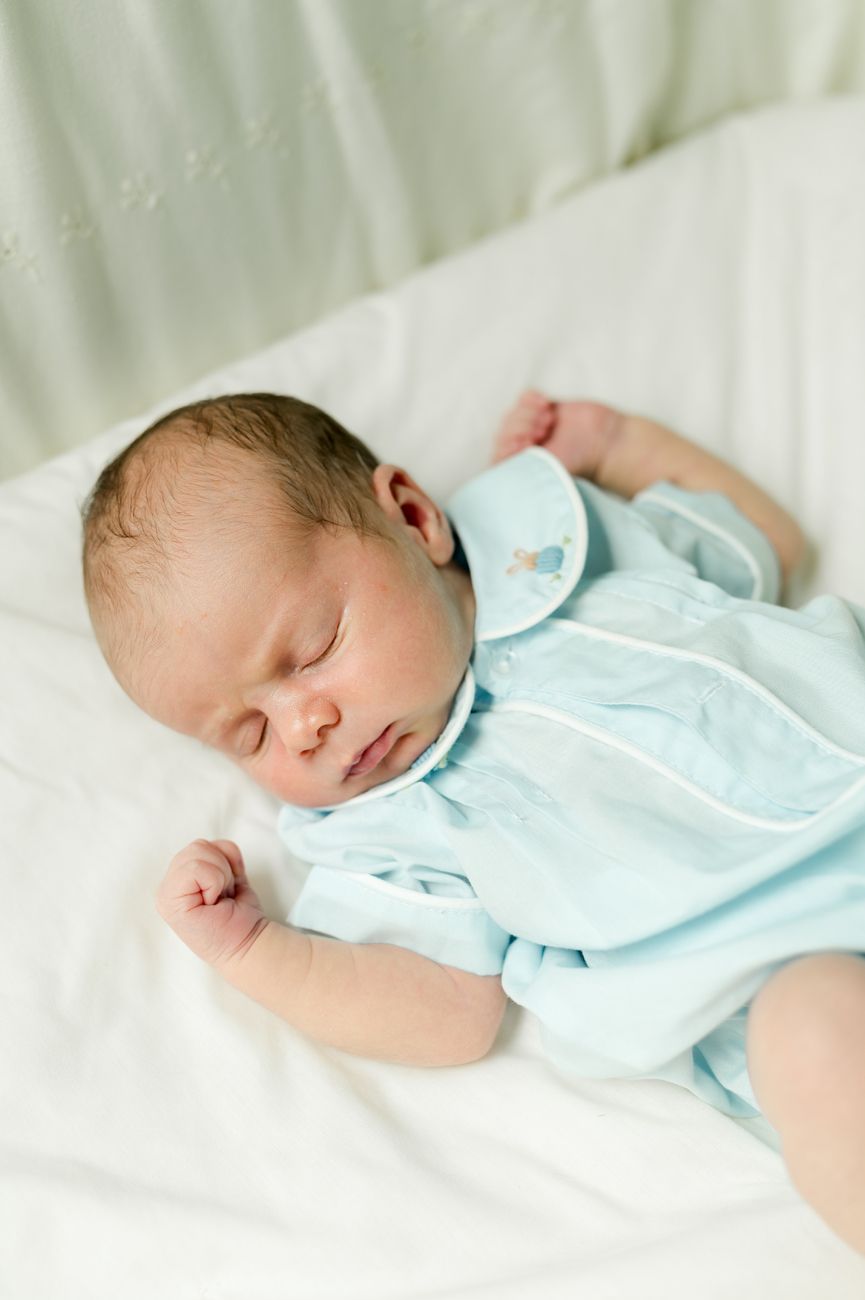 Sleeping infant wearing light blue outfit rests peacefully on white bedding.