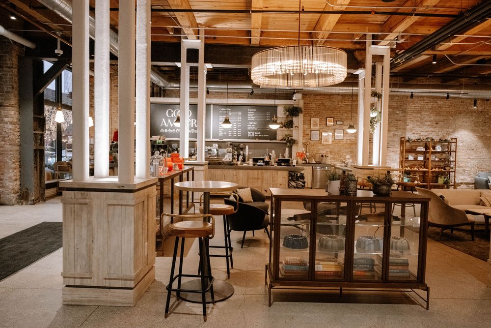 Modern rustic restaurant interior with exposed brick walls, wooden furniture, and an elegant crystal chandelier in warm lighting.